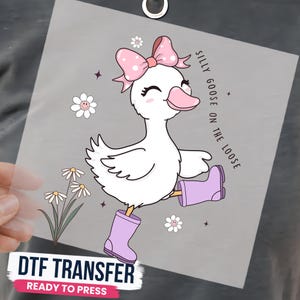 May include: A DTF transfer sheet featuring a white cartoon goose wearing light purple rain boots and a pink polka-dot bow. The design includes white daisy flowers with smiley faces, small stars, and the text SILLY GOOSE ON THE LOOSE.