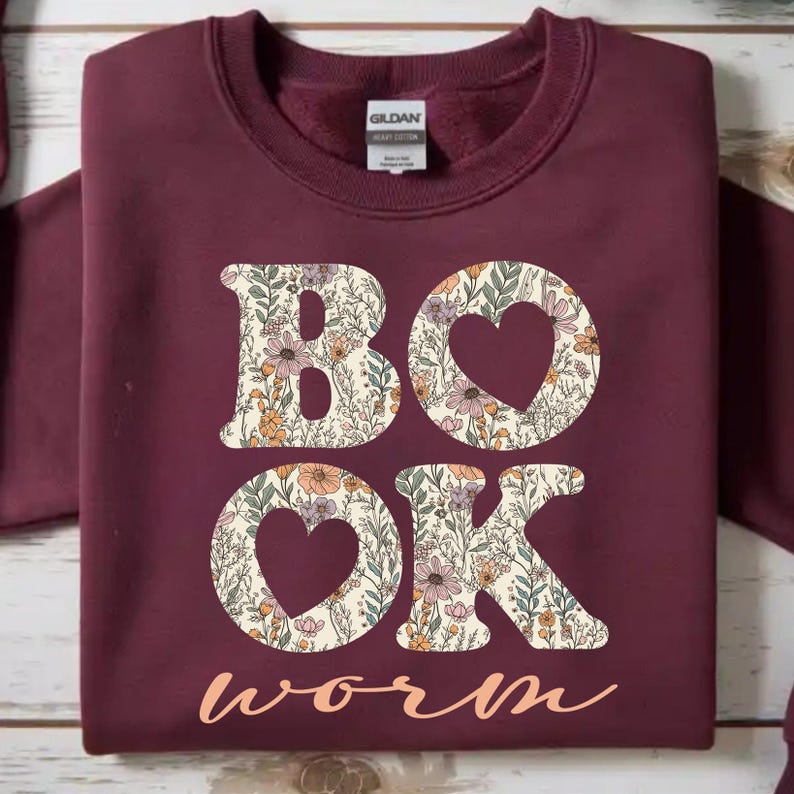 May include: Burgundy sweatshirt with the words "BOOK WORM" in a floral design. The letters "B" and "K" are filled with a floral pattern, and the "O"s are heart-shaped. The word "worm" is in a cursive font.