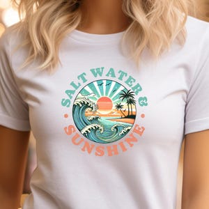 May include: White t-shirt with a graphic of a sunset over the ocean with waves and palm trees. The graphic is in a circle with the text "Salt Water & Sunshine" around it.