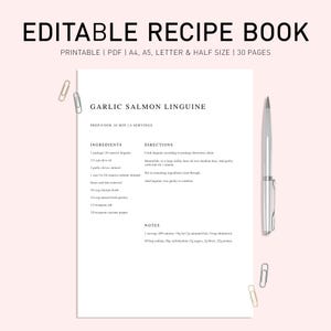 May include: A white recipe book page with the title "EDITABLE RECIPE BOOK" and a recipe for Garlic Salmon Linguine. A silver pen and paper clips are on the light pink background.