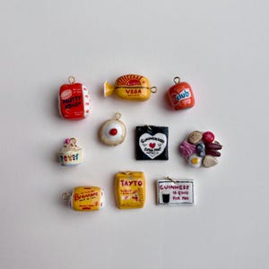 May include: A collection of ten miniature charms featuring various food and beverage brand logos and items, including Nutty Krust, Veda, Club, Mauds, a jam tart, a Guinness sign, a breakfast plate, Brennans, Tayto, and a Guinness is Good for You sign.