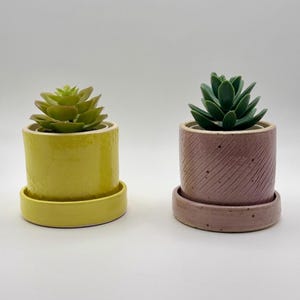 May include: A white ceramic mug with a black handle and the text "But First, Coffee" in a black, handwritten-style font. The mug is on a white surface.