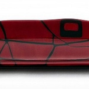 May include: A rectangular, red glass serving dish with a black geometric design. The dish has a slightly curved shape and is approximately 30 cm long. The black design features irregular lines and square shapes, creating a modern aesthetic.