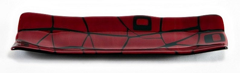 May include: A rectangular, red glass serving dish with a black geometric design. The dish has a slightly curved shape and is approximately 30 cm long. The black design features irregular lines and square shapes, creating a modern aesthetic.