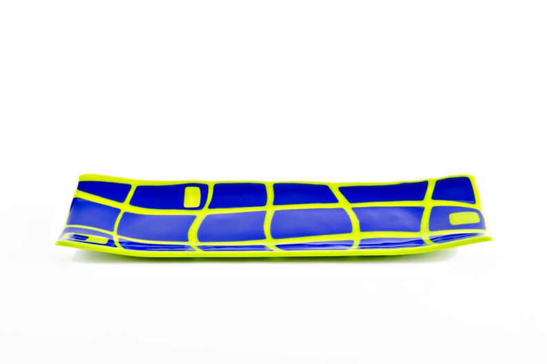 May include: A long, rectangular serving dish with a bold design. The dish has a blue interior with a grid pattern in bright yellow. The rim is also yellow, creating a striking contrast. The dish is ideal for serving snacks or small dishes.