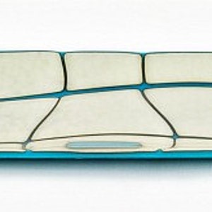 May include: A long, rectangular decorative tray with a unique design. The tray features a light cream-coloured surface divided into irregular shapes by dark grey lines. The edges and accents are a vibrant turquoise blue, creating a striking contrast.