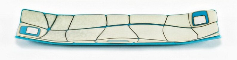 May include: A long, rectangular decorative tray with a unique design. The tray features a light cream-coloured surface divided into irregular shapes by dark grey lines. The edges and accents are a vibrant turquoise blue, creating a striking contrast.