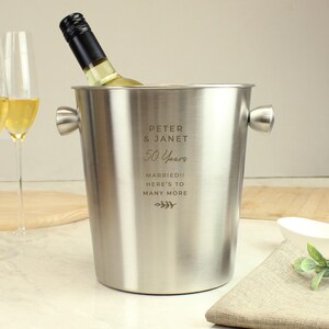 May include: A stainless steel wine bucket with two handles, holding a bottle of white wine. The bucket is engraved with "Peter & Janet 50 Years Married!! Here's to many more."