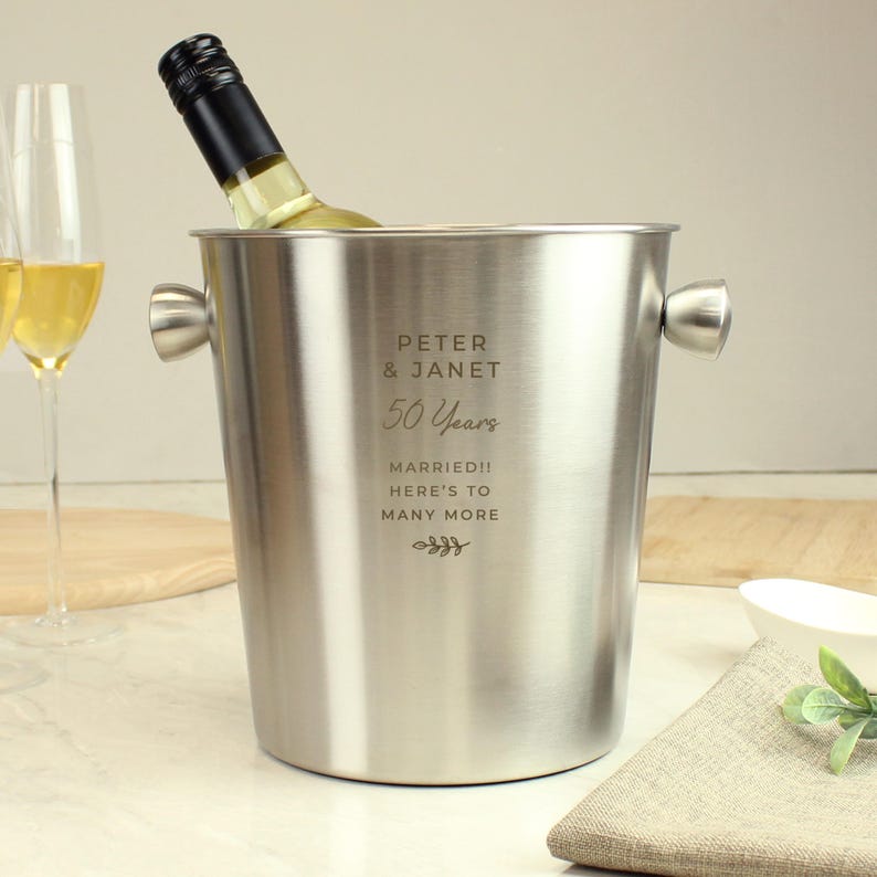 May include: A stainless steel wine bucket with two handles, holding a bottle of white wine. The bucket is engraved with "Peter & Janet 50 Years Married!! Here's to many more."