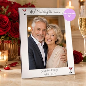 May include: Silver photo frame with the text "40th Wedding Anniversary" and the names "Jonathon & Amy 1984-2024". The frame has two champagne glasses at the top and bottom. The frame holds a photo of a smiling couple.