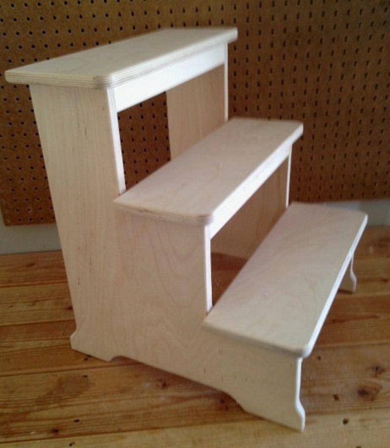May include: A three-step wooden stool made of light wood. The stool has a simple design with rounded edges and a natural finish.