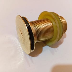Könnte beinhalten: Ein messingfarbener Ablaufstopfen mit einem Gewindekörper und einem kreisförmigen Kopf. Der Stopfen hat eine gelbe Gummidichtung und ist für den Einsatz in einem Waschbecken oder einer Badewanne konzipiert. Das Metall hat eine polierte Oberfläche.