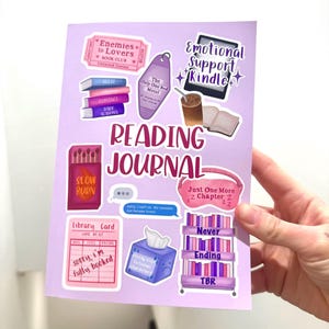 Op de afbeelding: Een lichtpaars leesdagboek met diverse stickers. Stickers zijn onder meer een boekenclubticket, een motelsleutel, een Kindle, een lucifersdoos, een bibliotheekkaart, een tissuebox en een boekenplank. Het dagboek wordt door een hand vastgehouden.