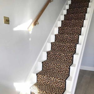 Könnte beinhalten: Eine Treppe mit einem Läufer im Leopardenmuster. Der Läufer hat einen schwarzen Rand und befindet sich auf einer weißen Treppe.