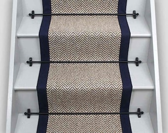 May include: A beige and brown herringbone patterned stair runner with navy blue edging. The runner is held in place with black metal rods.