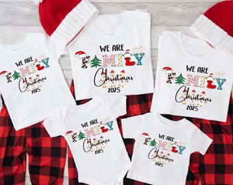 May include: A set of matching family Christmas pyjamas and hats. The white tops display the text "WE ARE FAMILY Christmas 2025" with festive designs. Red and black plaid pyjama bottoms and red knit hats complete the holiday set.