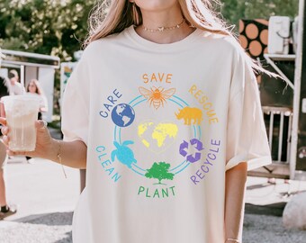 May include: White t-shirt with a colorful graphic design featuring a bee, rhino, turtle, tree, and the words "Save", "Care", "Clean", "Plant", "Rescue", and "Recycle".