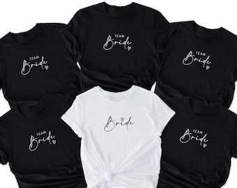 May include: Five black and white t-shirts with the text "Team Bride" in a script font. The shirts are arranged in a circle with the white shirt in the center.