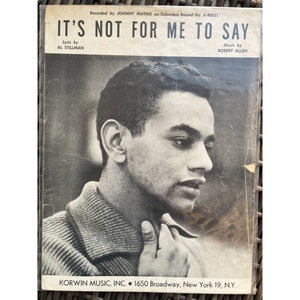 May include: A black and white photograph of a man with a serious expression. The photo is from a sheet music cover for the song "It's Not For Me To Say" by Johnny Mathis. The sheet music is credited to Al Stillman (lyrics) and Robert Allen (music). The sheet music is published by Korwin Music, Inc. and includes the address 1650 Broadway, New York 19, N.Y.