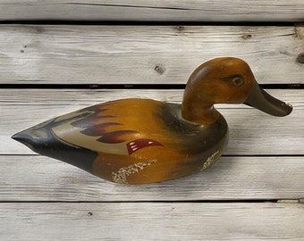 May include: A hand-painted wooden duck decoy with brown, black, and red accents. The decoy has a detailed design and is a great addition to any home decor.