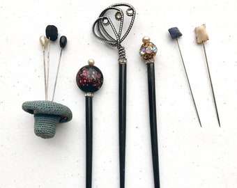 Puede incluir: Una colección de alfileres de sombrero y horquillas decorativas. Los alfileres presentan varios diseños, incluyendo un sombrero de ganchillo, detalles de perlas y cuentas, y adornos de joyería. Los alfileres son de varios colores, incluyendo negro, plata y oro.