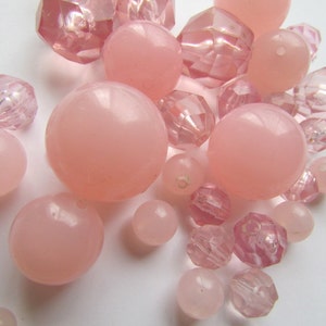 Puede incluir: Una colección de cuentas rosas de varios tamaños y formas. Algunas cuentas son redondas y opacas, mientras que otras están facetadas y translúcidas. La paleta de colores varía del rosa claro al medio, creando una estética suave y femenina. Ideal para la creación de joyas.