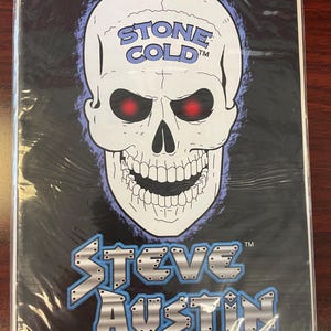 May include: A black comic book cover featuring a skull with red eyes and the words "STONE COLD" above it. Below the skull, the name "STEVE AUSTIN" is displayed in a stylized font. The word "PREVIEW" is at the bottom.