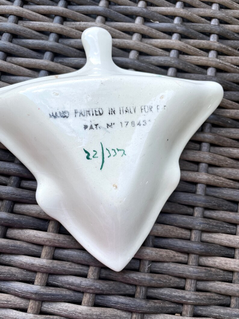 May include: A white, triangular ceramic dish with a handle, hand-painted in Italy. The dish has a unique shape and features text that reads "HAND PAINTED IN ITALY FOR F..." and "PAT. N&deg; 17843". The number "22/335" is also visible.