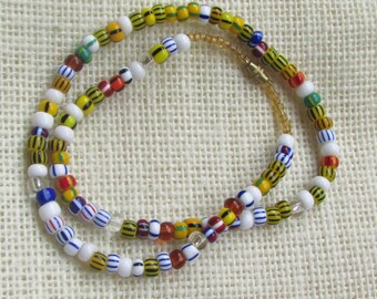 May include: A multi-strand necklace made of colorful glass beads. The beads are white, yellow, blue, red, and orange. The necklace is made of a variety of different sizes and shapes of beads.
