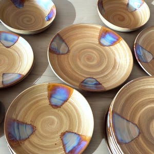May include: Set of brown ceramic plates with iridescent blue and purple accents. The plates have a swirl pattern and are perfect for serving meals.