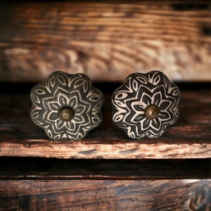 May include: Two black and white ceramic drawer knobs with a floral design. The knobs have a brass screw in the center.