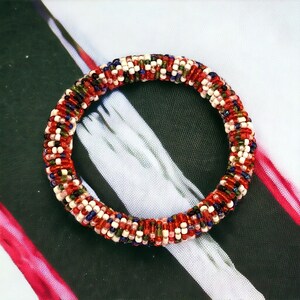 May include: A colorful beaded bracelet with red, white, blue, green, and brown beads. The bracelet is made of small, round beads that are woven together in a spiral pattern.