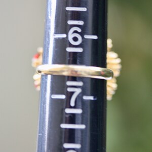 May include: A gold ring with red and white stones set in a floral design. The ring is sized on a ring sizer that shows the size is 7.