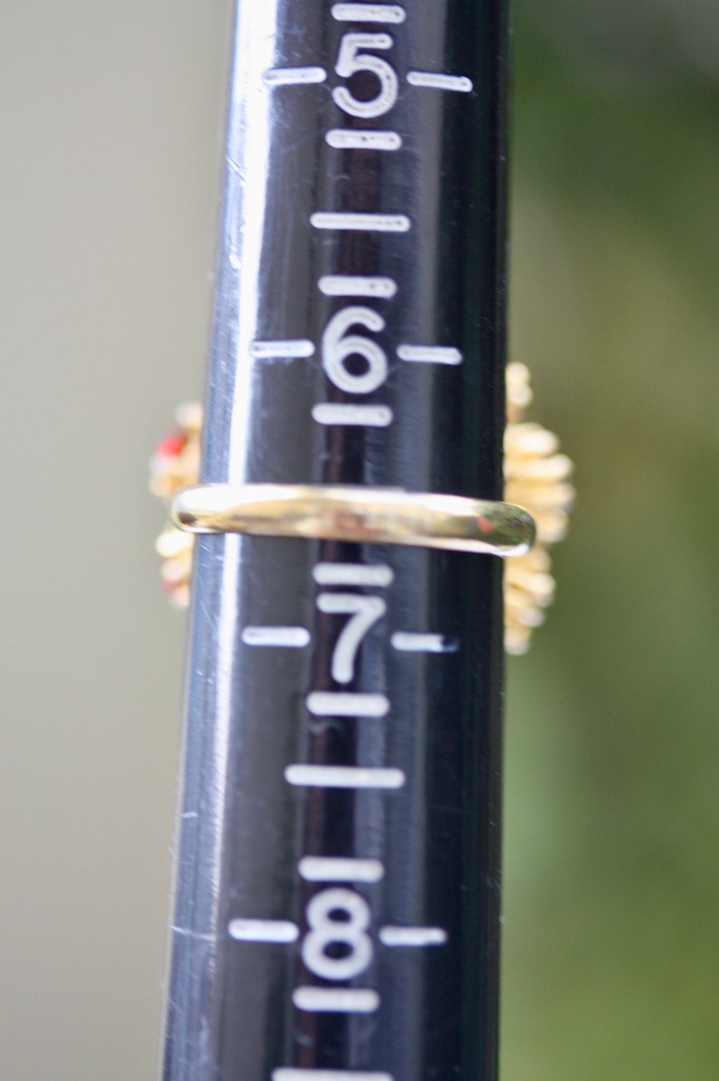 May include: A gold ring with red and white stones set in a floral design. The ring is sized on a ring sizer that shows the size is 7.