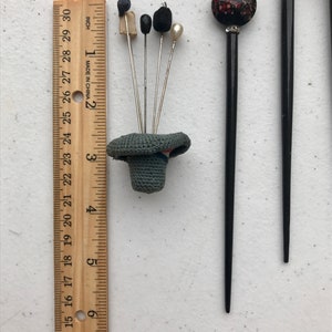 May include: A collection of vintage hat pins and hair sticks. The hat pins feature various decorative tops, including a small bird, black beads, and a pearl. A ruler shows the pins are approximately 3 inches (7.6 cm) tall.