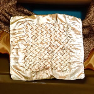 May include: A cream-colored satin pillow with a woven pattern. The pillow is made of soft, luxurious fabric and has a subtle sheen.