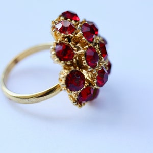 May include: A gold ring with a cluster of red gemstones. The ring is set with a large number of small, faceted stones.