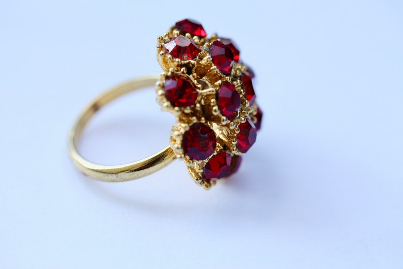 May include: A gold ring with a cluster of red gemstones. The ring is set with a large number of small, faceted stones.