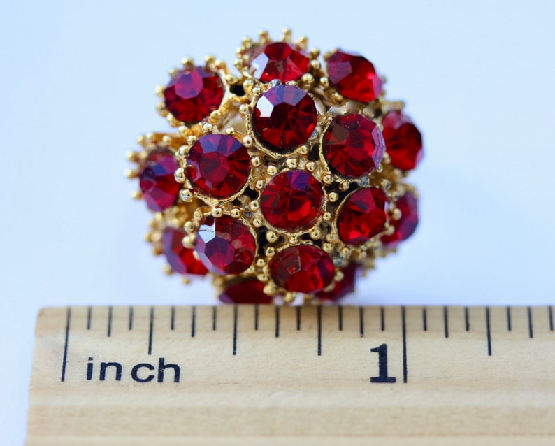 May include: A close-up of a red rhinestone ball ornament measuring 1 inch in diameter. The ball is made of many small red rhinestones set in gold metal.