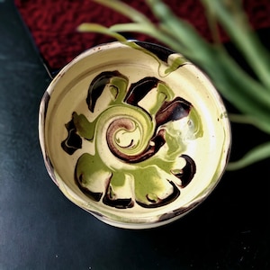 May include: A ceramic bowl with a swirling pattern of green, brown, and white glaze.