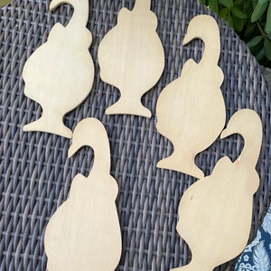 May include: Five unfinished wooden cutouts shaped like birds. The cutouts are arranged in a circle on a woven wicker surface.
