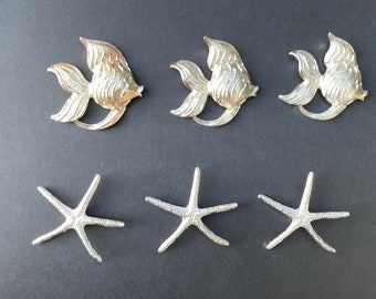 May include: Three silver fish ornaments and three silver starfish ornaments. The fish are stylised and have a textured surface. The starfish are simple and have five points.