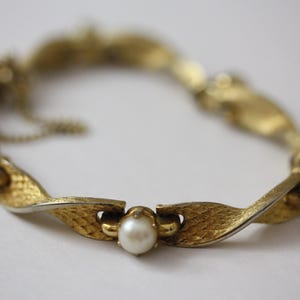 May include: A gold-tone bracelet with a twisted design and faux pearl accents.