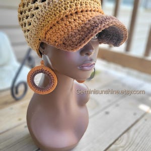 May include: A crocheted hat with a visor and matching hoop earrings. The hat and earrings are in shades of brown and tan. The hat has an open weave design. The earrings are large and circular. The website address Geminisunshine.etsy.com is visible.