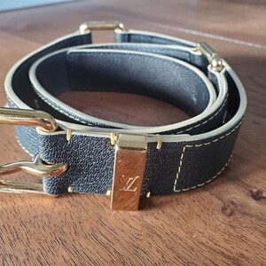 May include: A black leather belt with a gold buckle and a yellow stitching detail. The belt has a LV logo on the buckle.