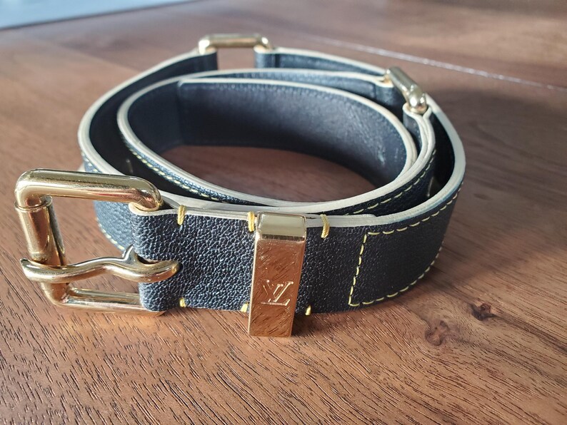 May include: A black leather belt with a gold buckle and a yellow stitching detail. The belt has a LV logo on the buckle.