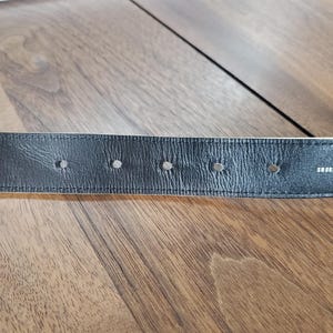May include: Close-up of a black leather belt with multiple holes and the word "SHOEBOX" embossed on the back.