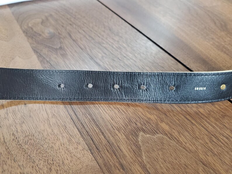 May include: Close-up of a black leather belt with multiple holes and the word "SHOEBOX" embossed on the back.