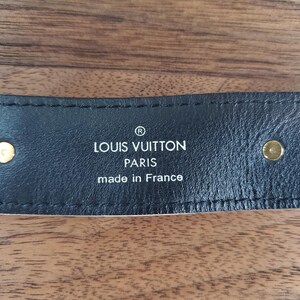 May include: Close-up of a black leather belt with gold hardware and the text "LOUIS VUITTON PARIS made in France" embossed in white.