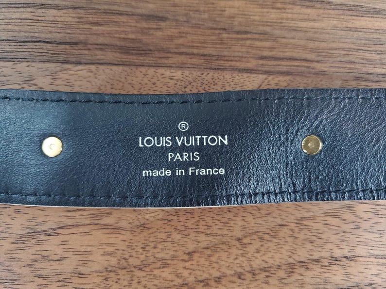 May include: Close-up of a black leather belt with gold hardware and the text "LOUIS VUITTON PARIS made in France" embossed in white.
